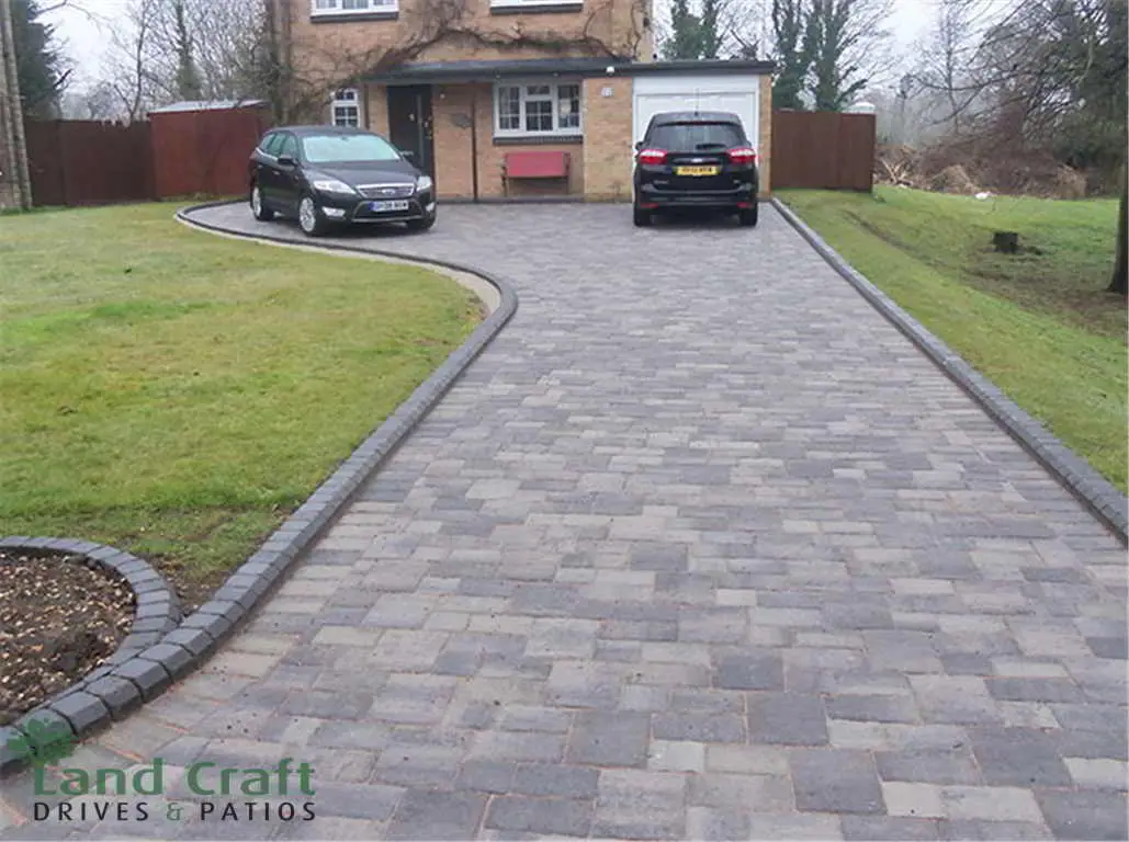 Grey block paved driveway curving between lawns