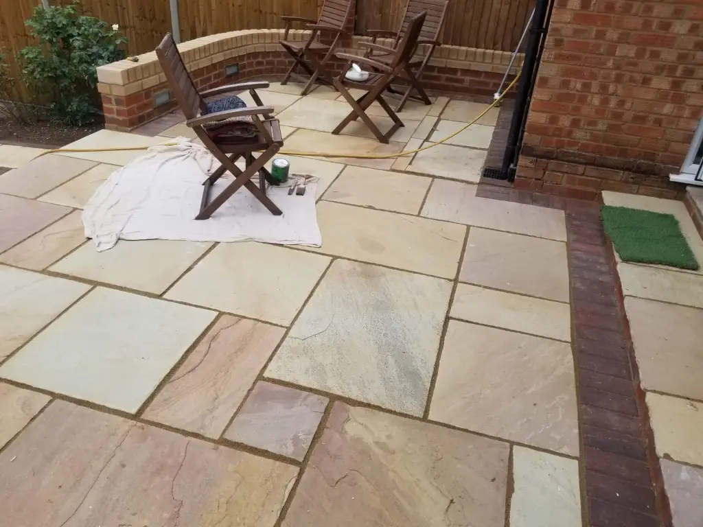 Sandstone patio with a brick border and garden furniture